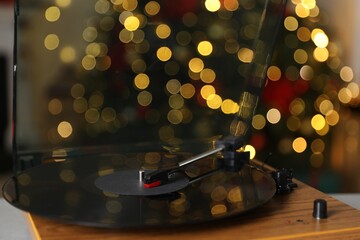 Turntable with vinyl record on table near Christmas tree, closeup