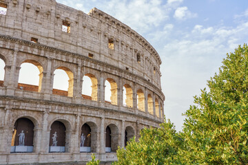 Fototapeta premium Rome, Italy. Ancient Colosseum (Coliseum) stands majestically against blue sky, surrounded by lush greenery, showcasing historical architecture and cultural significance