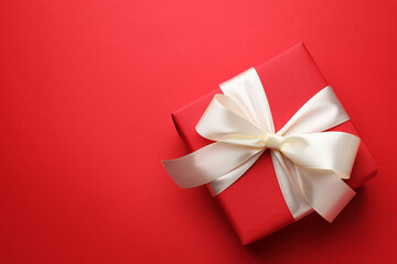 Beautiful gift with bow on red background, top view