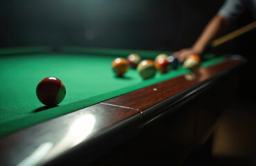 Player aims cue stick at billiard balls on green felt table. Colorful spheres arranged for game, focused on pocketed or soon to be pocketed ball. Indoor leisure activity in club.