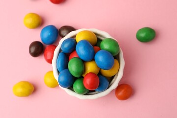 Delicious colorful candies in bowl on pink background, flat lay