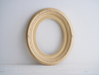 Antique ivory oval picture frame with ornate details, leaning on a white textured wooden surface against a light gray wall, with copy space in the center.