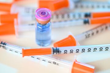 Close up of Pile of Single Use Syringes with Orange Safety Tips and Glass Vials
