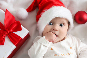 Baby in Santa hat, Christmas gift and baubles on bed, top view