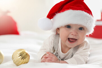 Baby in Santa hat and Christmas baubles on bed