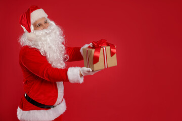 Santa Claus with Christmas gift on red background, space for text