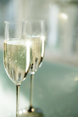 Two filled champagne glasses on a modern glass table. Elegant modern style with soft bright green background und light bokeh. Vertical close-up.
