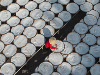 Aerial view of a worker in a conical hat tending to numerous trays filled with white contents, creating a geometric pattern of light and shadow, Tay Ninh, Tay Ninh, Vietnam.