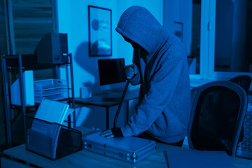 Thief trying to open locked briefcase with crowbar in office at night