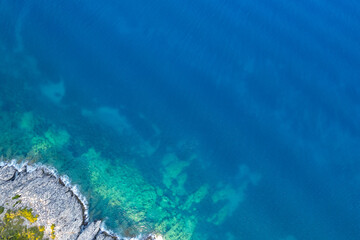 Drone aerial view of turquoise sea water meeting a rocky coastline on a sunny summer day