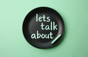 Black plate with lets talk about chalk text on green background. Encourages conversation, sharing feelings, and open dialogue about mental wellness and other subjects.