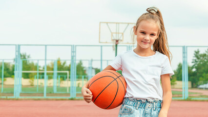 Portrait girl basketball player holding a basketball ball looking at the camera standing on the basketball court outdoors. Concept of sport, active lifestyle. Sports and recreation