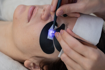 A woman undergoing eyelash extension procedure using an ultraviolet lamp.