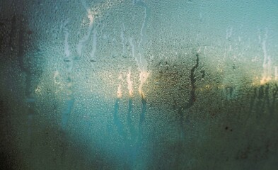 Abstraktes Motiv mit beschlagener Glasscheibe und Wasserstreifenmuster vor Baum und goldgelb-blauem Himmel bei Frost und K&auml;lte bei Sonnenaufgang am Morgen im Winter