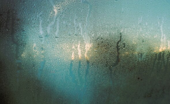 Abstraktes Motiv mit beschlagener Glasscheibe und Wasserstreifenmuster vor Baum und goldgelb-blauem Himmel bei Frost und K&auml;lte bei Sonnenaufgang am Morgen im Winter