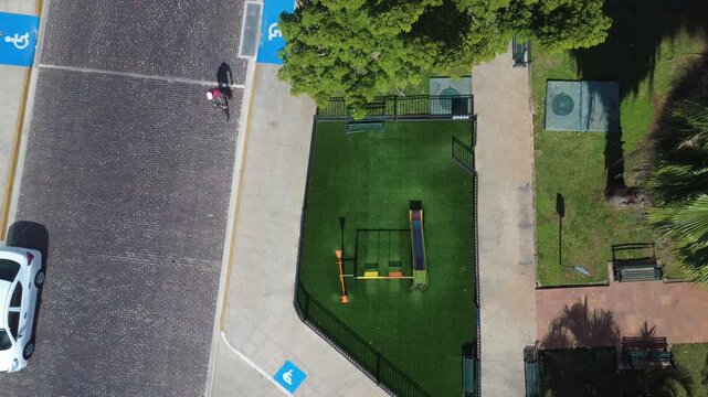 4K drone top-down view showing a colorful playground with swings and a slide in La Ermita, M&eacute;rida, surrounded by urban textures and greenery.