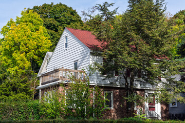 Suburban house with red roof and balcony amid early autumn trees in Brighton, Boston area, Massachusetts, USA
