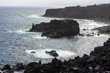 Rocky volcanic headland on the misty north coast of Tenerife with waves breaking against dark cliffs.