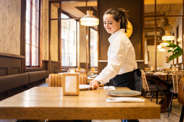 A young woman between 20 and 30 years old with Down syndrome is working as a waitress in a...