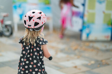 Toddler Girl Wearing a Helmet and Riding a Bright Pink Balance Bike Outdoors