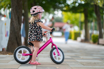 Toddler Girl Wearing a Helmet and Riding a Bright Pink Balance Bike Outdoors