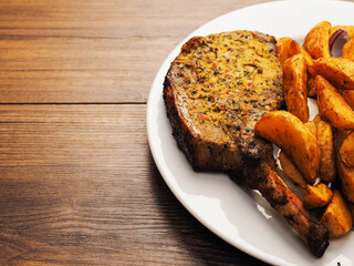 Fine dinner with spicy pork chop, potato wedges and fresh tomato on a plate on a wooden table. Tasty meal with meat and vegetables.