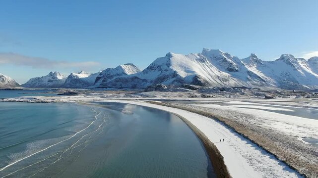 A drone captures the snowy winter beach at Fredvang in the Lofoten Islands, where turquoise waters meet white sand under a deep steel-blue sky - surreal and breathtaking.