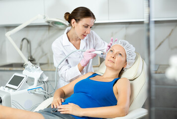 Fototapeta premium Professional female cosmetologist doing hydrafacial procedure in modern cosmetology clinic. Doctor use hydrogen and oxygen small bubbles for deeply clear skin. Rejuvenation and hydratation