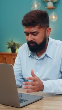 Indian man at home sees laptop error rubs forehead sighs upset virus glitch causing serious trouble. Arabian guy at table frustrated seeks quick fix hopes system recovers rapidly stress growing today.