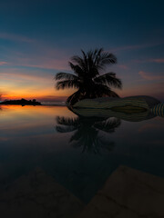 View from luxury villa at dusk, pool lighting, sun loungers for sunbathing, umbrellas from the sun, pillows for swimming in the pool, palm tree on background