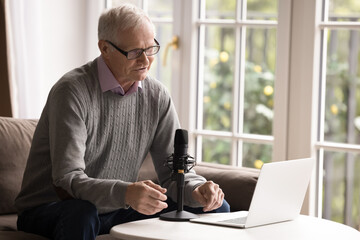 Tech savvy retired speaker. Busy senior man professional work online from comfy home office using notebook talk into condenser microphone record tutorial vlog take part in webinar video call meeting