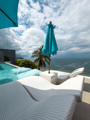 View from luxury villa at sunny day, sun loungers for sunbathing, umbrellas from the sun, pillows for swimming in the pool, palm tree on background