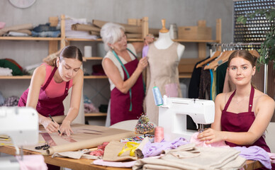 Mature fashion designer works with a mannequin and inspects sewn clothes next to a team of dressmakers in a garment factory. Workshop on sewing clothes