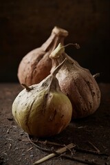 Three unique, dried gourd-like objects are arranged on a dark, earthy surface, creating a rustic still life. Their textured, weathered appearance, in tones of brown, beige, and subtle green, is accent