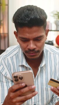 Indian man at home uses smartphone plus credit card to place order enters cvv and smiles after checkout. Arabian guy on sofa confirms order sees app status waits for delivery and feels safe payment