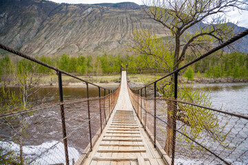 Fototapeta premium Wooden suspension footbridge crossing Chulyshman river near Katu Yaryk pass Altai Russia Remote connection point in wild mountain region