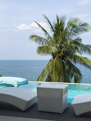 View from luxury villa at sunny day, sun loungers for sunbathing, umbrellas from the sun, pillows for swimming in the pool, palm tree on background