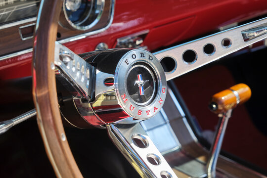 Closeup of the red interior and steering wheel with wood of an oldtimer Ford Mustang with the classic logo with horse in the center of the steering wheel