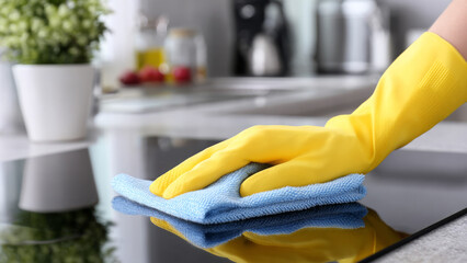 Person wearing yellow rubber gloves is cleaning a modern kitchen countertop with a blue microfiber cloth, showcasing effective cleaning techniques and a tidy environment