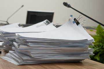 Huge stacks of paper documents with binder clips on a desk in a conference room with microphones. Concept of bureaucracy and budget reporting. Photo