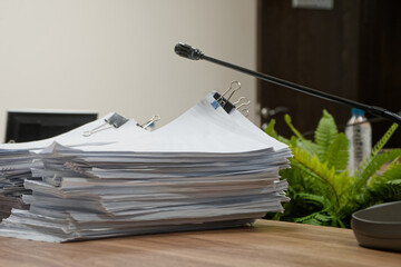 Huge stacks of paper documents with binder clips on a desk in a conference room with microphones. Concept of bureaucracy and budget reporting. Photo