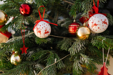 Snow-dusted green branches hold classic ornaments of white balls with red reindeer, golden and red balls, and small star pendants in a warm festive light