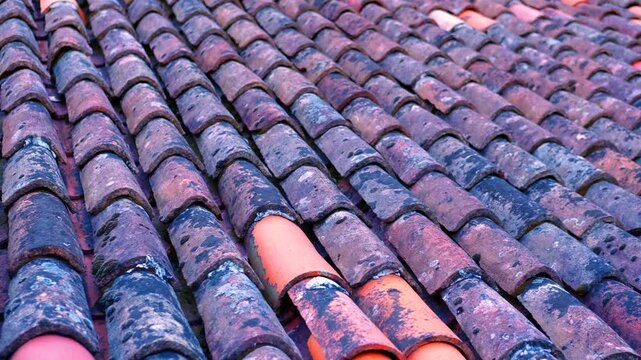 Old terracotta clay roof tiles pattern. Weathered terracotta roof tiles with moss and lichen creating a textured pattern. Old clay tile roof surface showing its age, offering an abstract background