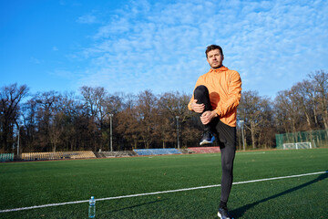 Man stretching leg while standing on sports field at outdoor stadium