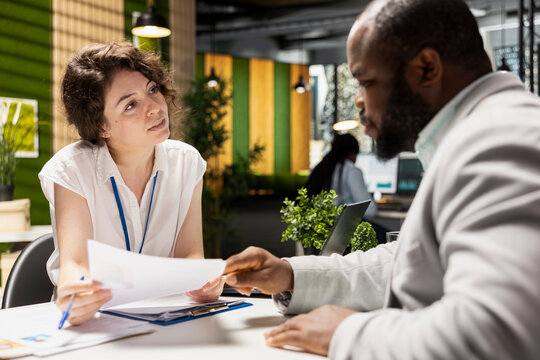Female HR recruiter speaking with black man job seeker in office, discussing CV resume feedback during formal interview, asking questions to ensure a successful meeting for career development.