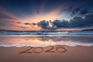 Happy New Year 2026 concept, text lettering on the beach sand at sea sunrise, tropical island sunset and ocean waves