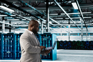 Data center engineer using laptop to automate errors detection for improved reliability and uptime. Server hub IT expert looking for network issues affecting rigs, performing database backups