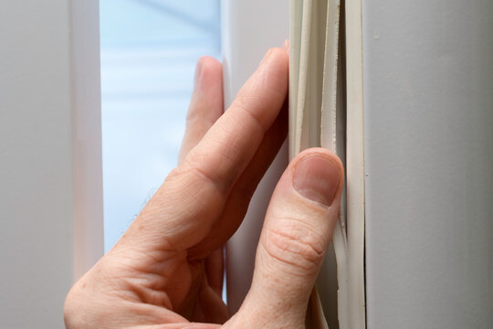 Hand shows torn refrigerator door gasket in closeup, highlighting worn rubber seal that causes cold leak and need for repair at home