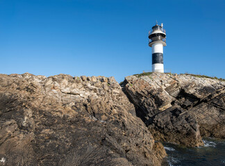 black and white lighthouse standing on a rocky cliff by the deep blue sea under a clear sky, Isla Pancha, Ribadeo, Galicia, Spain