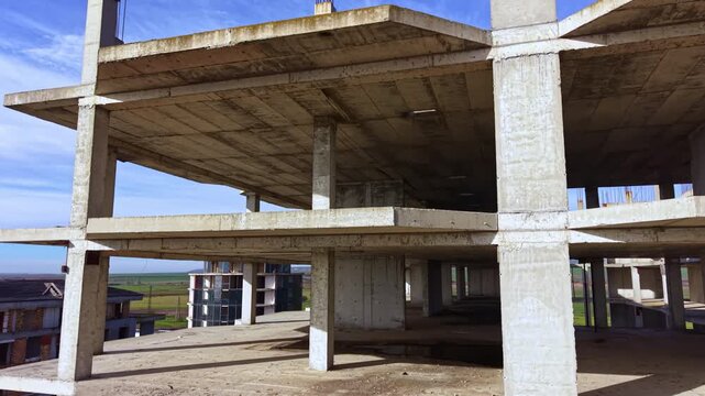 A large, unfinished structure rises against a vivid blue sky, revealing its bare concrete floors and expansive view of the surrounding landscape, hinting at untold stories of ambition and abandonment.